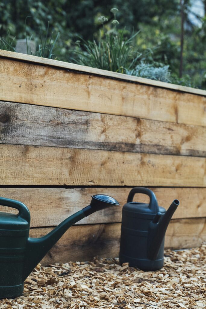Hochbeet befüllen und pflegen: grüne Gießkanne hängt an einer Holzwand im Garten