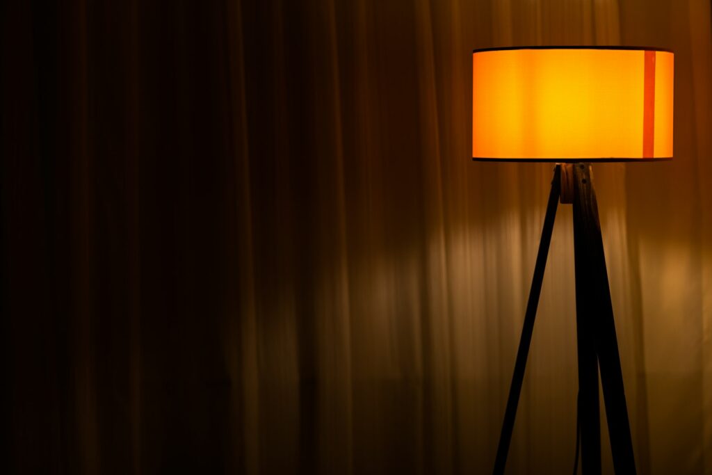 Lichtkonzept Wohnzimmer: eingeschaltete Tischlampe vor braunem Vorhang als warmes Akzentlicht