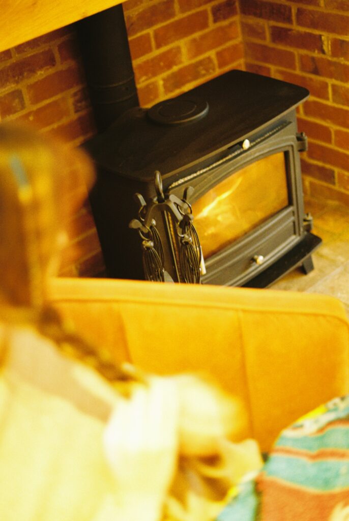 Wohnzimmer mit Kamin: gusseiserner Holzofen in einer Backsteinnische, davor ein Sessel